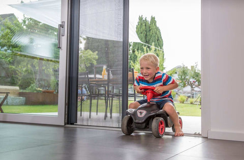 Child riding a toy car near Plissee insect protection door mounted on a door frame.