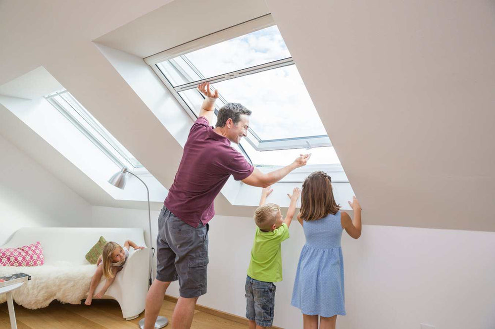 Person installing Insektenschutzrollo RO4/3 on a skylight window with children watching.